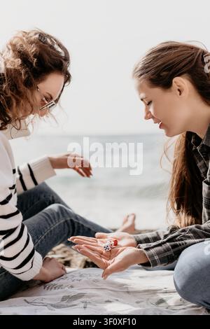 Women beach dice friends enjoying a sunny day outdoors while sitting on a blanket together by the calm ocean waves Stock Photo