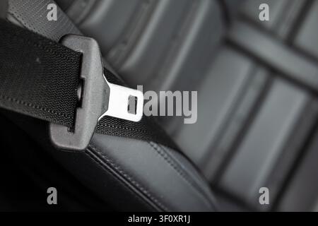 Extreme close-up macro shot captures the metallic finish of a seat belt buckle release, positioned against the clean, textured black leather surface o Stock Photo