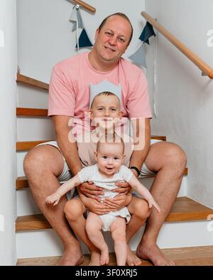 father and two children sitting together on a wooden staircase, creating a warm and familial atmosphere in an indoor setting. The scene is captured Stock Photo