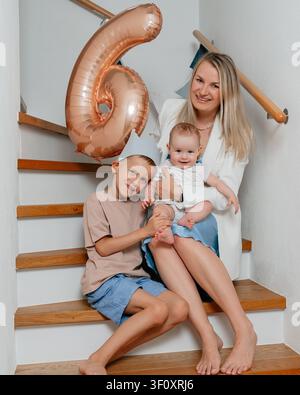 Family sitting on stairs, in staircase with wooden steps and white walls, with balloon, wooden staircase, white wall, with wood staircase, plastic Stock Photo