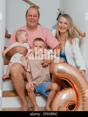 a heartwarming family portrait of a man holding a baby girl, a woman sitting next to a boy, and the boy in front of the man, all sitting together on a Stock Photo