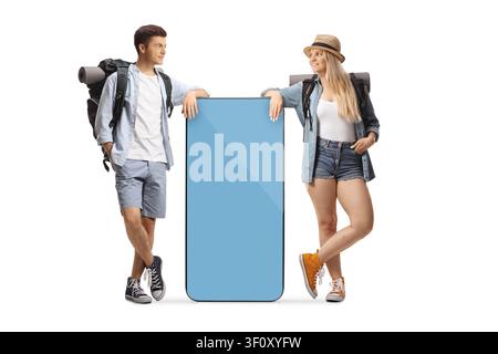 Young backpackers leaning on a big smartphone with a blank screen isolated on white background Stock Photo