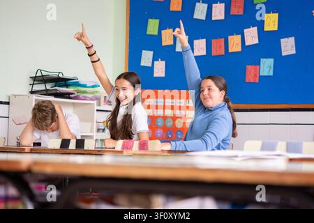 Elementary school students raising their hands while participating in a classroom lesson. Stock Photo