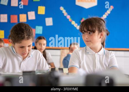 Elementary school classmates talking and collaborating during a lesson in a bright classroom. Stock Photo