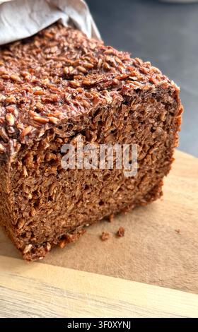 Freshly baked seed bread loaf with a textured crust, sliced and resting on a wooden cutting board Stock Photo