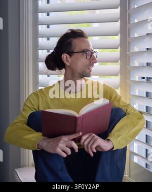 Portrait of Man Reading Book by Window With Content Expression Stock Photo