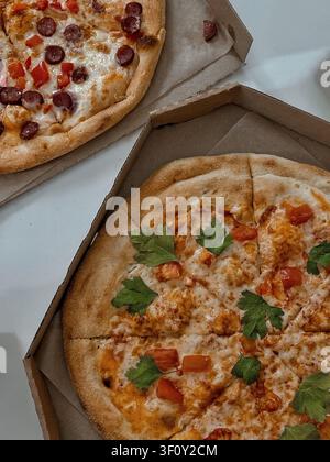 Two freshly baked pizzas served in open cardboard boxes on a white table, featuring pepperoni and chicken toppings in natural indoor lighting. Stock Photo