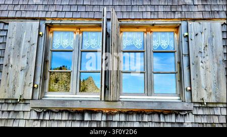 Weathered Wooden Shingle Wall of an Alpine Hut with Window Reflecting Blue Sky in the Bernese Oberland, Switzerland Stock Photo