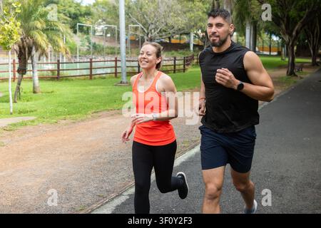 Happy athletic couple jogging together in a green park during an outdoor fitness workout Stock Photo