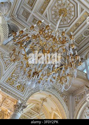 Saint Petersburg, Russia: May 8 2022 - Low angle view of a magnificent golden chandelier with crystal pendants hanging from a decorated geometric Stock Photo