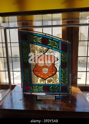 An intricate, historic stained glass panel depicting a coat of arms with three roses, displayed inside a glass museum showcase. Stock Photo