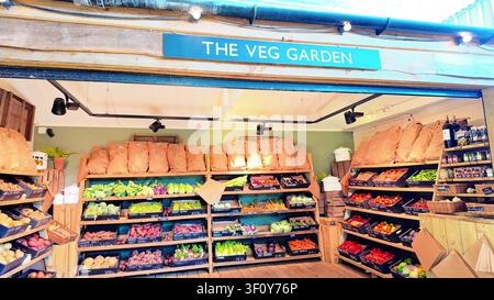 Rustic farm shop display counter under wooden canopy named "The Veg Garden" featuring fresh seasonal vegetables in crates. Stock Photo