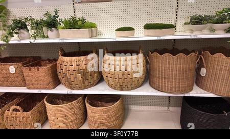 A selection of decorative woven wicker storage baskets and small artificial plants displayed on retail shelves inside a department store Stock Photo