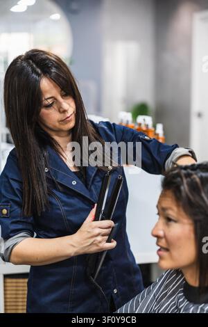 Hairdresser styling woman's hair with straightening iron Stock Photo