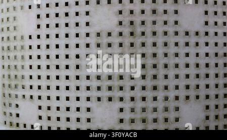 white plastic surface with a regular grid of small square holes. The material shows signs of wear, gray dust, and a light dark coating inside Stock Photo