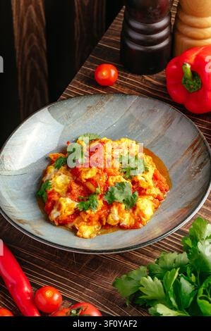 Savory scrambled eggs with tomato on a rustic table Stock Photo