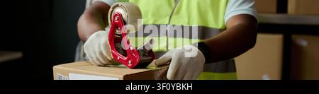 Header of worker sealing cardboard box with packing tape, preparing shipment in warehouse. Suitable for e commerce, logistics, order fulfillment, delivery service marketing Stock Photo