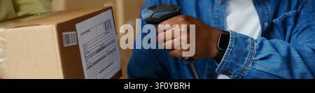 Header of of Black adult worker scanning shipping label on cardboard box with barcode reader, processing parcel for order fulfillment. Ideal for ecommerce logistics marketing Stock Photo