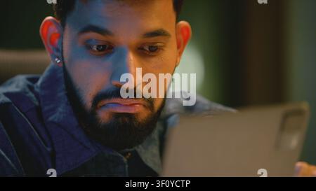 Close up Indian emotional astonish business man looking in digital tablet at night office Arabian businessman amazed with financial result Hindu male Stock Photo