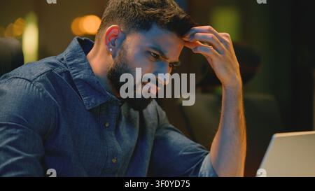 Pensive stressed irritated Indian business man angry with laptop difficult work at night office tired Arabian businessman Hindu male suffer with Stock Photo