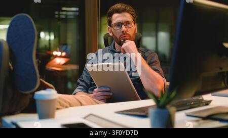 Pensive Caucasian business man thinking idea writing notes looking in computer at night office thoughtful businessman analyst male executive think Stock Photo