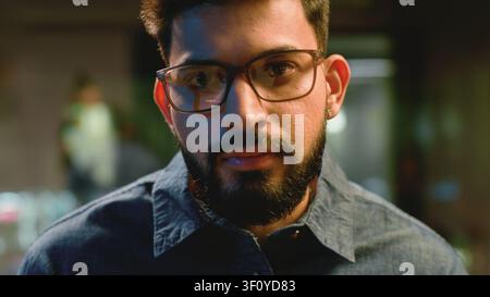 Indian business man working at night in office computer lights reflection in glasses. Arabian ethnic businessman male guy programmer trader wear Stock Photo