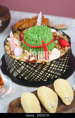 A cake is placed on a table decorated with green icing. Nearby, there are various snacks and a glass of tea. The scene shows a festive setup for a cel Stock Photo