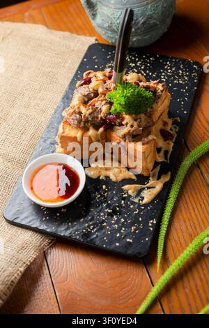 This dish features thick slices of bread topped with various ingredients and sauce. It is served on a black plate, highlighting the rich colors of the Stock Photo