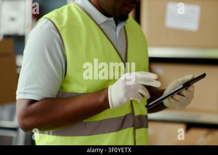 Close up of Black middle aged warehouse worker using tablet while checking inventory in storage area, supporting logistics management, supply chain marketing, fulfillment services Stock Photo