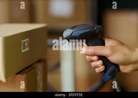 Close up of adult hand scanning barcode on cardboard box with handheld reader, managing warehouse inventory and order tracking. Ideal for logistics, retail, shipping content Stock Photo