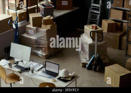 High angle shot of warehouse packing station with wrapped pallets, boxes, laptop, monitor, hard hat, supporting logistics workflow and inventory control. Ideal for supply chain marketing Stock Photo