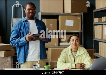 Portrait of African American man and biracial woman managing inventory with tablet and laptop in warehouse office. Supporting ecommerce operations, fulfillment workflow, small business marketing Stock Photo