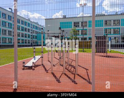 Outdoor gym equipment behind metal fence in schoolyard. Stock Photo