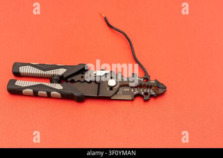 Wire Stripper Stripping Electrical Wire on Red Background, Industrial Wire Stripper Tool Gripping Black Cable on Vibrant Red Background. Stock Photo