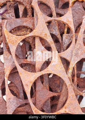 Close-up of rusty metal industrial scraps with circular cutout patterns. Corroded steel texture, abstract geometric shapes, weathered metal background, oxidation, recycling concept, grunge surface, industrial waste, detailed macro. Stock Photo