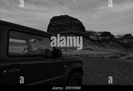 4x4 stands on Iceland's winter moorland, dwarfed by the dramatic volcanic dome of Lómagnúpur in b&w Stock Photo