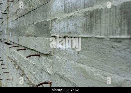 Perspective view of a rough concrete wall with sticking rusty rebar. Stock Photo