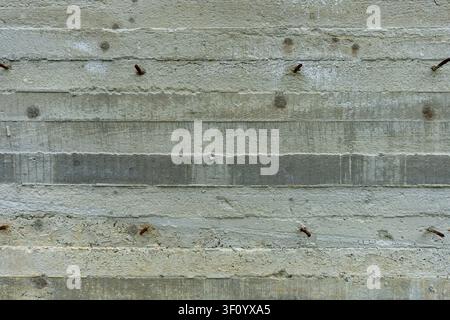 Rough textured concrete wall with horizontal board marks and rusty rebar. Stock Photo