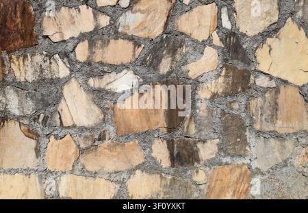 Natural stone wall with flat quatzite stones assembled in cement mortar. Warm colors that go from light yellow to brown. Background and texture. Stock Photo