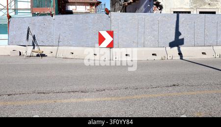 Traffic direction sign on oriented stranded board barrier with large building under renovation behind. Street in front. Background for copy space. Stock Photo