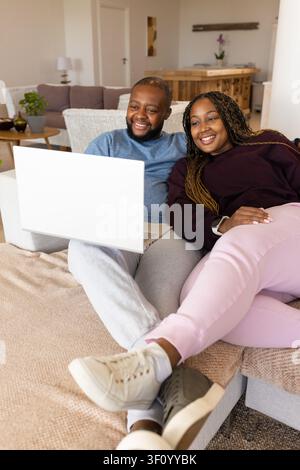 African couple sitting on light-colored sectional sofa, leaning close and viewing white laptop Stock Photo