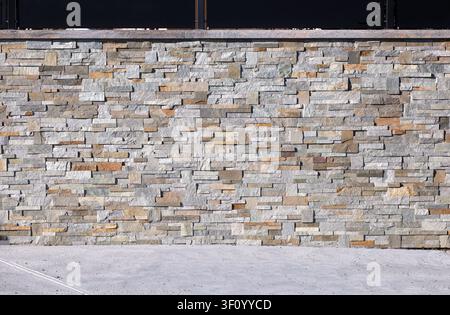 Fence made of faux stone veneer wall and black metal paneling on top . Concrete flooring. Background and texture. Stock Photo
