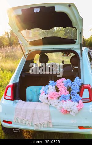 Scenic outdoor composition featuring a flower-filled car trunk in warm sunset light, symbolizing freedom, road trips and summer celebrations Stock Photo