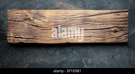 An old oak board on a dark stone table. A template for varied arrangement of objects or food. Top view. Stock Photo