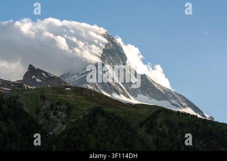 Matterhorn mountain with clouds passing over its snowy slopes and green hills below Stock Photo