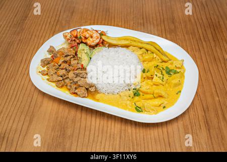 Hearty Mixed Platter Featuring White Rice, Beef Stew, Shrimp Cocktail, Yellow Curry, Avocado and Fried Plantains Served on Oval Plate Stock Photo