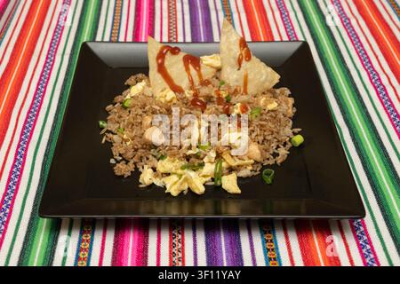 Chicken Fried Rice with Scrambled Eggs and Wonton Chips Served on a Black Square Plate Over a Colorful Striped Tablecloth Stock Photo