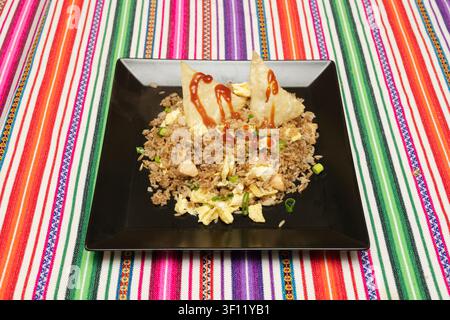 Chicken Fried Rice with Scrambled Eggs and Crispy Wonton Chips Served on a Black Plate Over a Colorful Striped Tablecloth Stock Photo