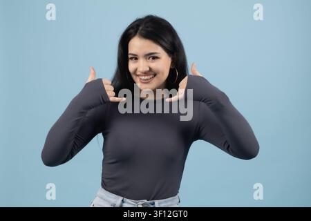 Young woman framing face with hands smiling looking positive Stock Photo