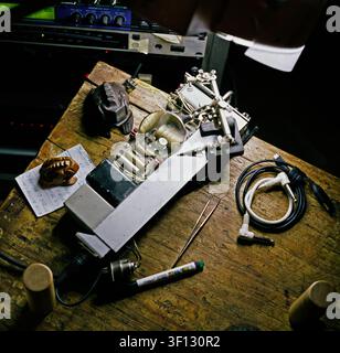 Cluttered workbench in a music studio with a magnifying glass enlarging part of a printed circuit board under task lighting, analog photography. Stock Photo